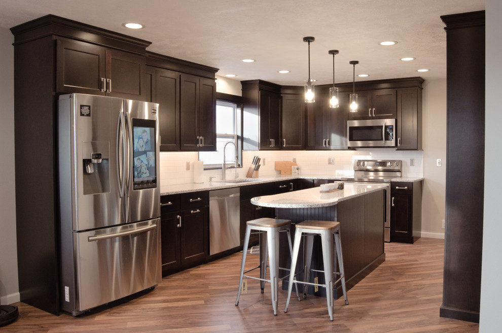 Example of a l-shaped kitchen design with a single-bowl sink, shaker cabinets, dark wood cabinets, granite countertops, white backsplash, stainless steel appliances and an island