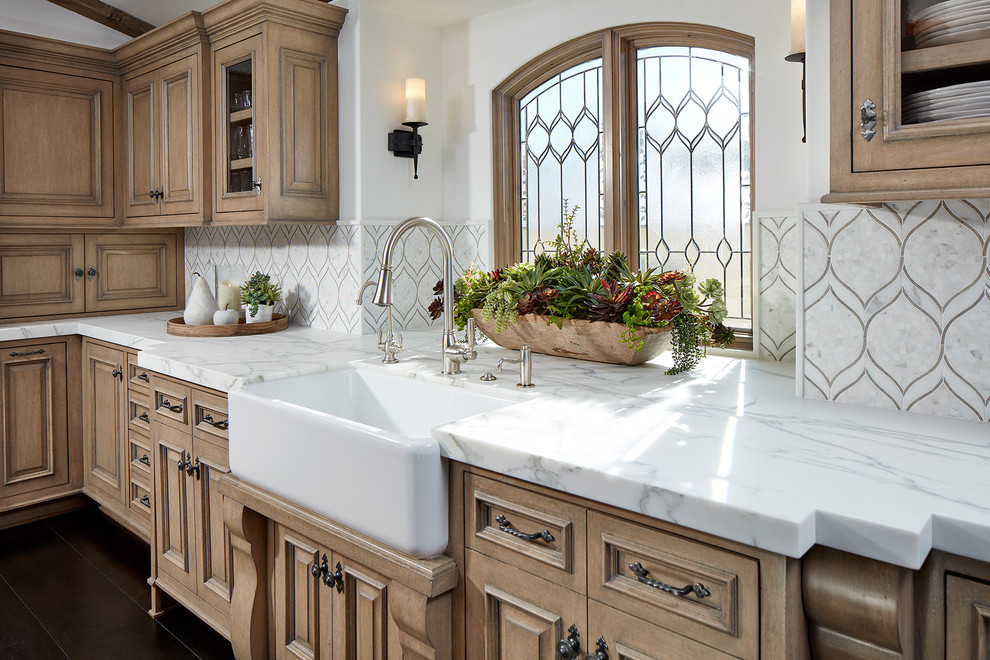 Design ideas for a large beach style u-shaped eat-in kitchen in Orange County with a farmhouse sink, glass-front cabinets, beige cabinets, marble benchtops, white splashback, stone tile splashback, stainless steel appliances, dark hardwood floors, with island and brown floor.
