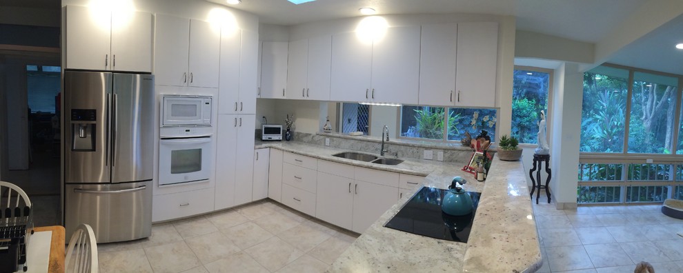 Inspiration for a large transitional l-shaped eat-in kitchen in Hawaii with a double-bowl sink, flat-panel cabinets, white cabinets, granite benchtops, beige splashback, stone slab splashback, stainless steel appliances, ceramic floors, a peninsula, beige floor and beige benchtop.