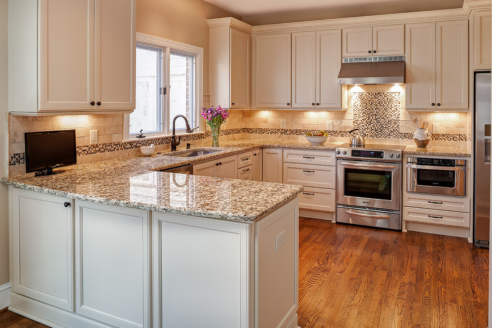 Photo of a small traditional u-shaped eat-in kitchen in Charlotte with a single-bowl sink, flat-panel cabinets, white cabinets, granite benchtops, beige splashback, stone tile splashback, stainless steel appliances, medium hardwood floors and a peninsula.