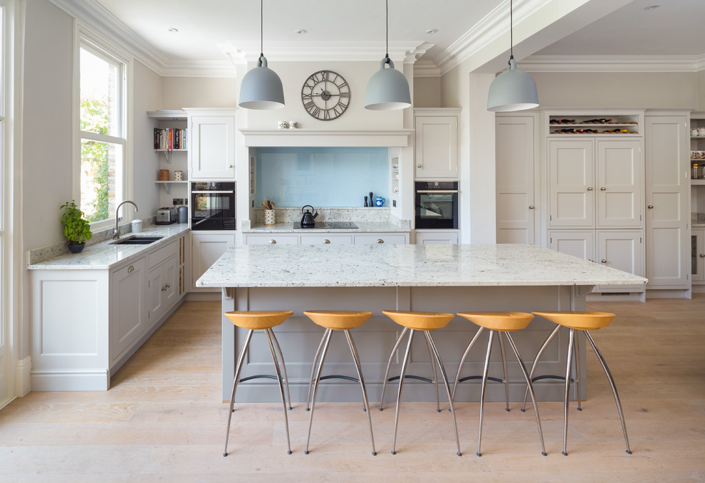 Photo of a large transitional u-shaped open plan kitchen in Other with a drop-in sink, shaker cabinets, beige cabinets, marble benchtops, beige splashback, marble splashback, black appliances, light hardwood floors, with island, beige floor and beige benchtop.
