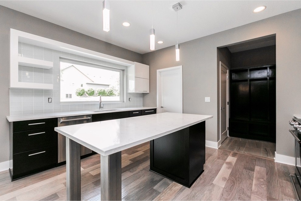 Mid-sized minimalist galley light wood floor and gray floor eat-in kitchen photo with a single-bowl sink, flat-panel cabinets, dark wood cabinets, quartzite countertops, white backsplash, glass tile backsplash, stainless steel appliances and an island
