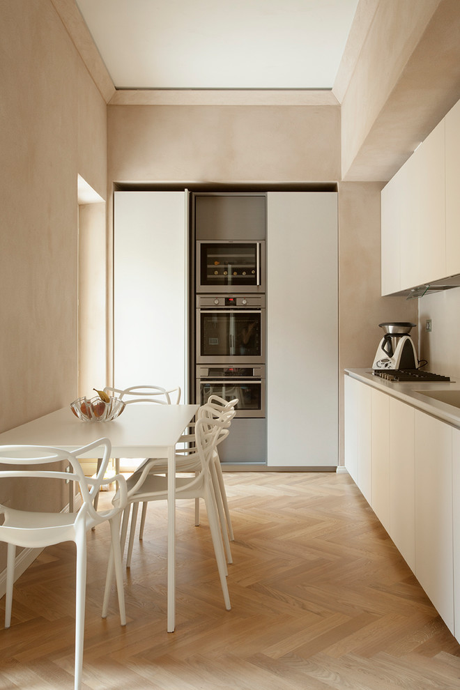 Photo of a mid-sized modern single-wall separate kitchen in Turin with flat-panel cabinets, no island, an integrated sink, beige cabinets, beige splashback, stainless steel appliances, light hardwood floors, beige floor and beige benchtop.