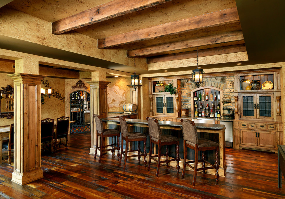 Expansive country u-shaped seated home bar in Cincinnati with recessed-panel cabinets, medium wood cabinets, brown splashback, stone tile splashback, dark hardwood floors and brown floor.