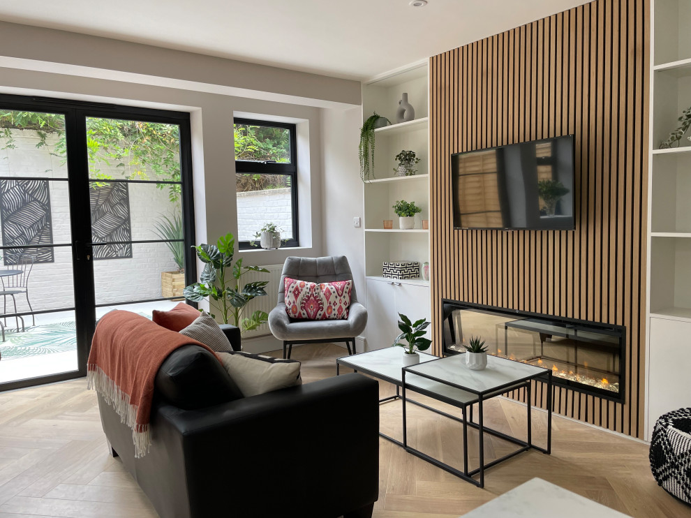 Modelo de salón abierto actual de tamaño medio con paredes beige, suelo de madera en tonos medios, pared multimedia, suelo beige y panelado