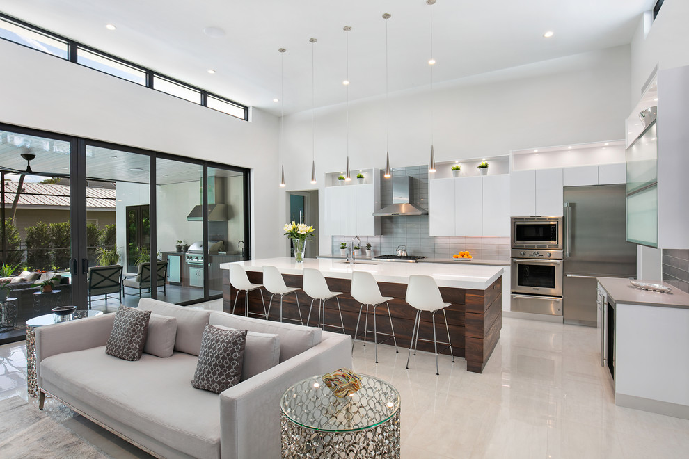 Inspiration for a large modern l-shaped open plan kitchen in Tampa with an undermount sink, flat-panel cabinets, white cabinets, quartz benchtops, grey splashback, glass tile splashback, stainless steel appliances, porcelain floors, with island, white floor and grey benchtop.