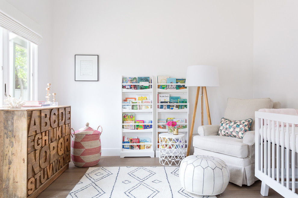 Photo of a transitional nursery for girls in Los Angeles with white walls and light hardwood floors.