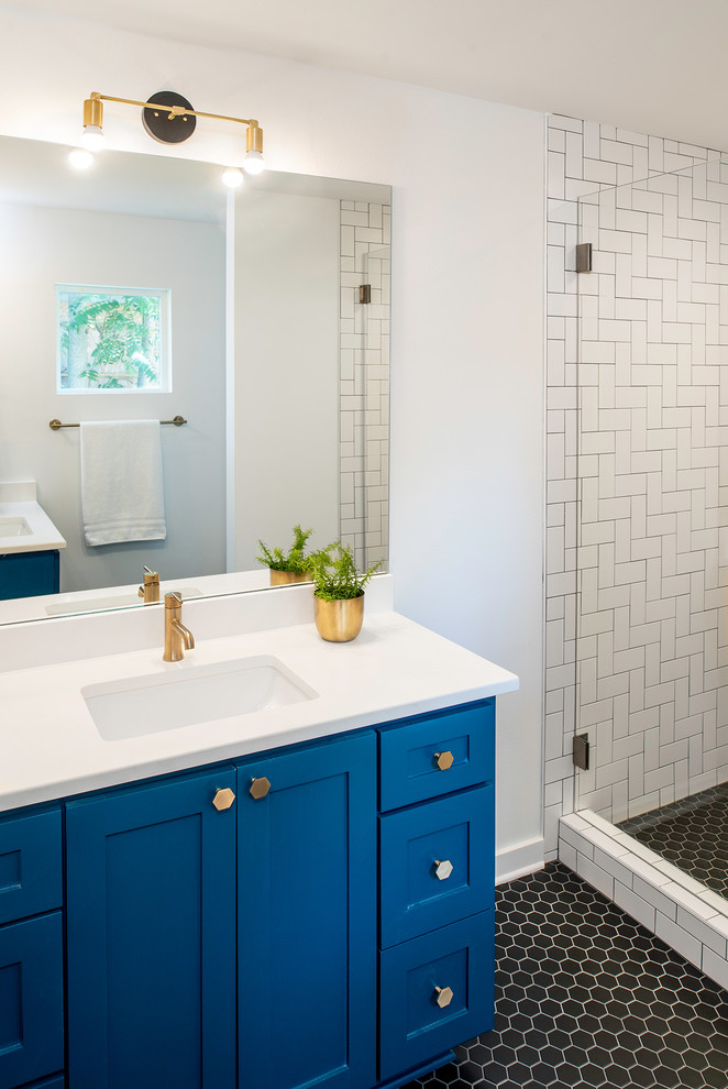 Photo of a mid-sized transitional 3/4 bathroom in Austin with shaker cabinets, blue cabinets, an alcove shower, white tile, porcelain tile, white walls, porcelain floors, an undermount sink, solid surface benchtops, black floor and white benchtops.