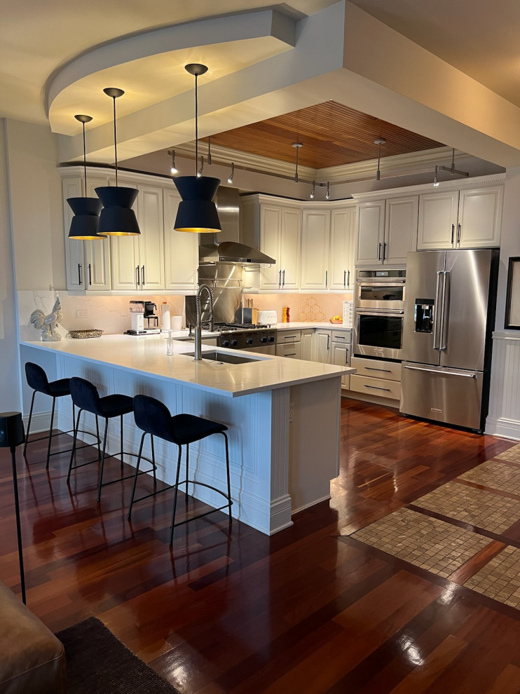 Example of a minimalist u-shaped dark wood floor, brown floor and coffered ceiling kitchen design in Chicago with an undermount sink, raised-panel cabinets, gray cabinets, quartz countertops, white backsplash, quartz backsplash, stainless steel appliances and white countertops