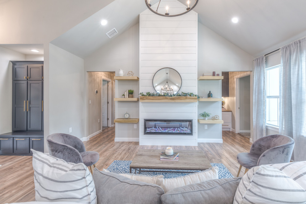 This is an example of a country open concept living room in Other with grey walls, laminate floors, a wood fireplace surround and brown floor.