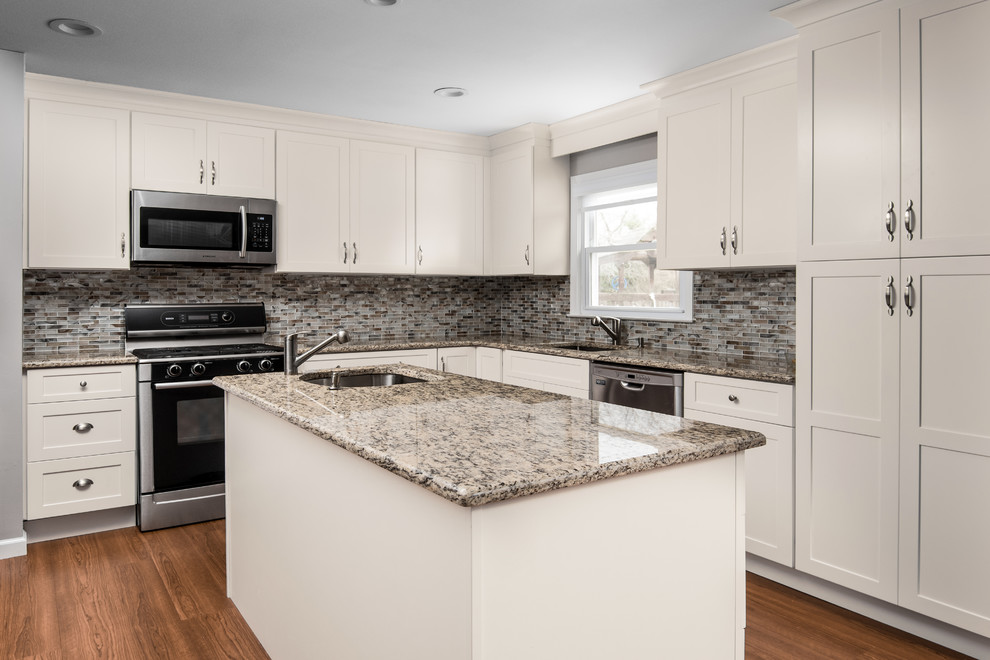 This is an example of a mid-sized traditional u-shaped kitchen in New York with an undermount sink, shaker cabinets, white cabinets, granite benchtops, brown splashback, glass tile splashback, stainless steel appliances, medium hardwood floors, with island, blue floor and brown benchtop.