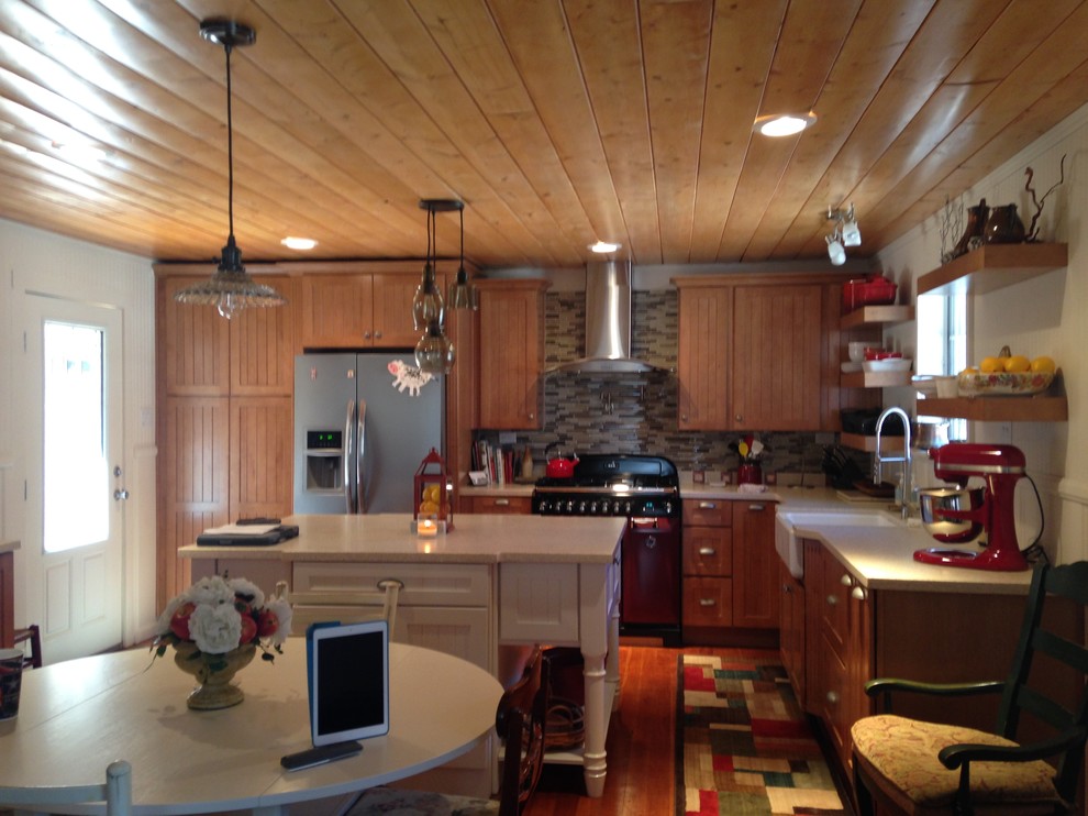 Example of a mid-sized mountain style l-shaped medium tone wood floor open concept kitchen design with a farmhouse sink, beaded inset cabinets, light wood cabinets, solid surface countertops, beige backsplash, glass tile backsplash, stainless steel appliances and an island