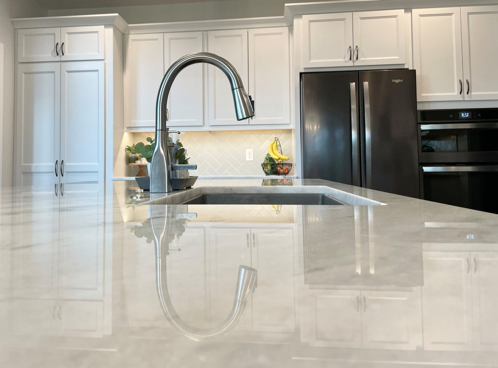 This is an example of a large traditional l-shaped open plan kitchen in Other with a submerged sink, flat-panel cabinets, white cabinets, marble worktops, white splashback, metro tiled splashback, black appliances, an island and white worktops.