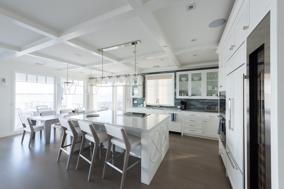 Design ideas for a mid-sized beach style l-shaped open plan kitchen in New York with an undermount sink, white cabinets, blue splashback, glass tile splashback, stainless steel appliances, medium hardwood floors, with island, brown floor, white benchtop and shaker cabinets.