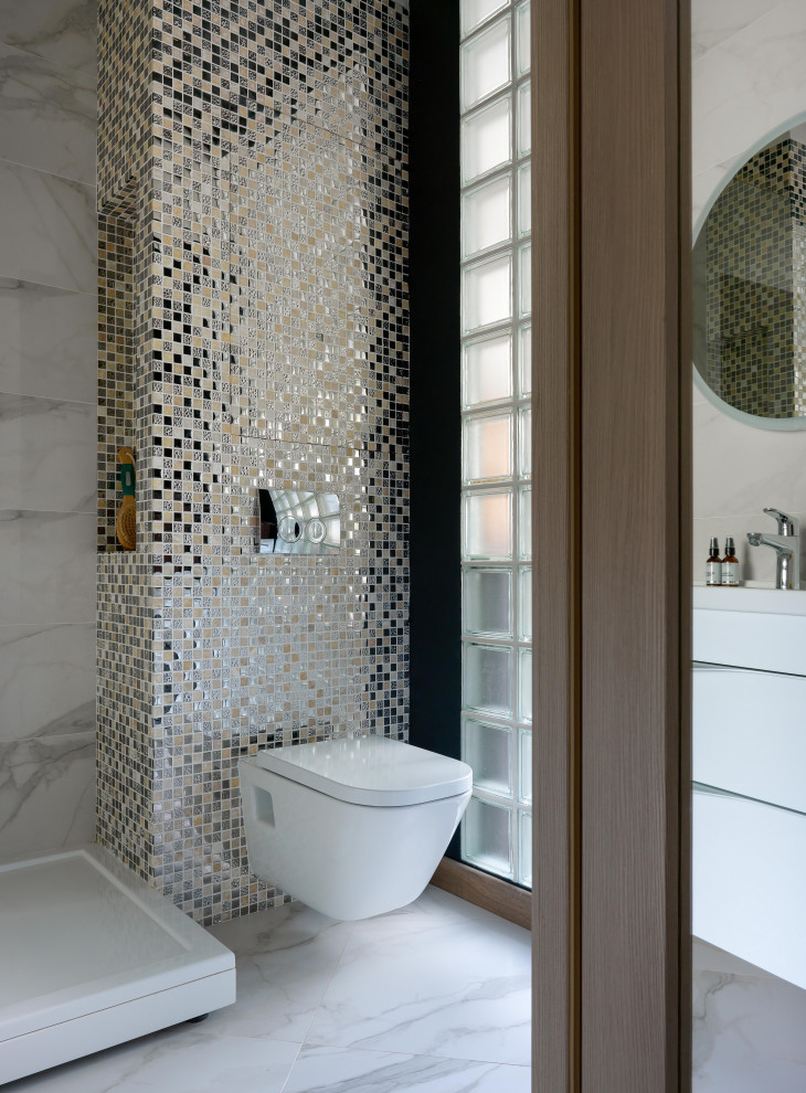 Modern inredning av ett litet badrum, med klinkergolv i keramik, släta luckor, vita skåp, en hörndusch, en vägghängd toalettstol, flerfärgad kakel, mosaik och vitt golv