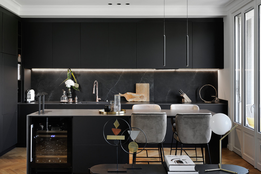 Inspiration for a contemporary open plan kitchen in Lyon with flat-panel cabinets, black cabinets, black splashback, stone slab splashback, light hardwood floors, with island and grey benchtop.