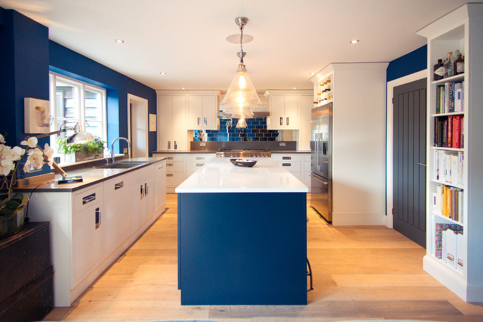 Inspiration for a transitional u-shaped kitchen in Other with an undermount sink, flat-panel cabinets, white cabinets, blue splashback, subway tile splashback, light hardwood floors and with island.