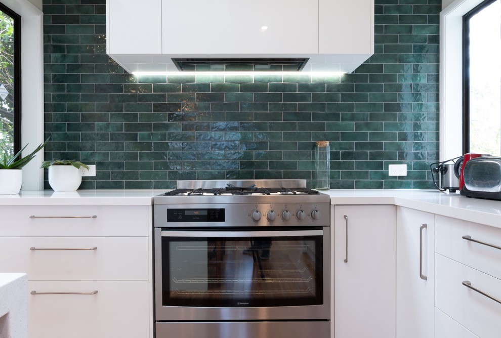 Photo of a large modern u-shaped eat-in kitchen in Auckland with an integrated sink, open cabinets, white cabinets, quartz benchtops, green splashback, ceramic splashback, stainless steel appliances, dark hardwood floors, with island and white benchtop.