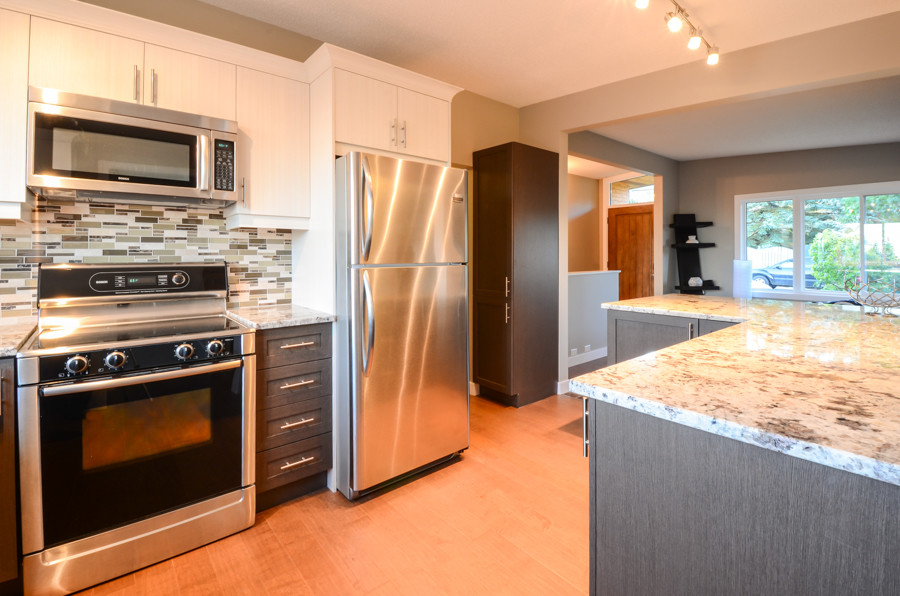 Inspiration for a small transitional l-shaped medium tone wood floor open concept kitchen remodel in Calgary with an undermount sink, shaker cabinets, dark wood cabinets, marble countertops, multicolored backsplash, matchstick tile backsplash, stainless steel appliances and an island