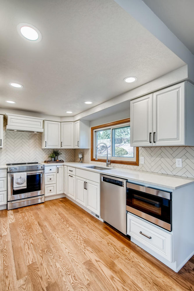 Photo of a mid-sized traditional u-shaped eat-in kitchen in Denver with a single-bowl sink, raised-panel cabinets, white cabinets, quartz benchtops, yellow splashback, ceramic splashback, stainless steel appliances, light hardwood floors and white benchtop.