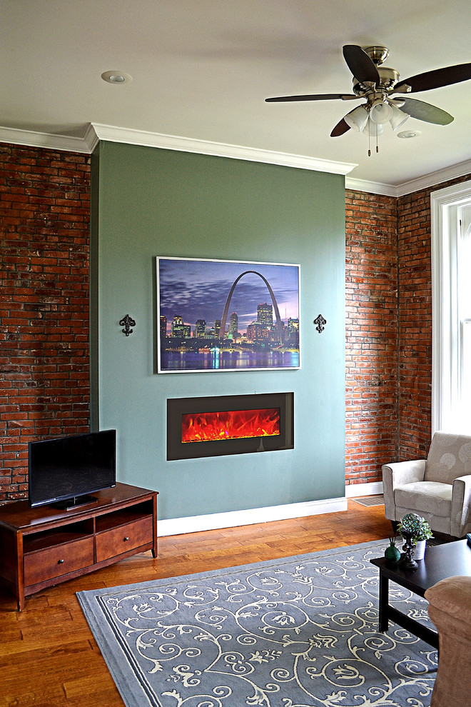 Photo of a small traditional formal enclosed living room in St Louis with red walls, medium hardwood floors, a hanging fireplace, a metal fireplace surround, a freestanding tv and beige floor.
