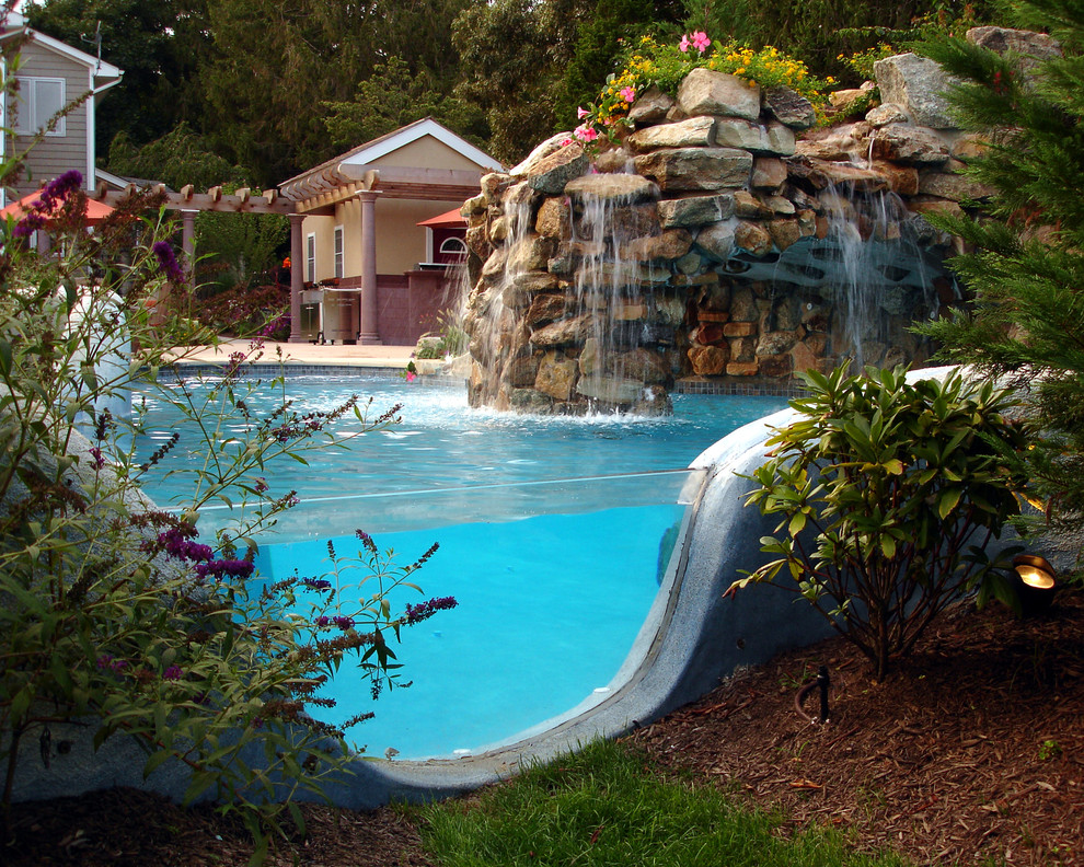 Photo of a large tropical backyard custom-shaped lap pool in New York with a water feature and concrete slab.