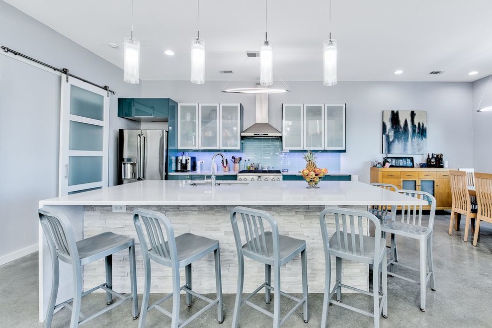 Transitional galley eat-in kitchen in New Orleans with an undermount sink, flat-panel cabinets, blue cabinets, blue splashback, glass tile splashback, stainless steel appliances, concrete floors, with island, grey floor and white benchtop.