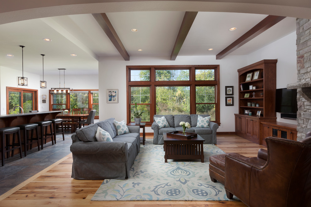 Design ideas for a large arts and crafts open concept family room in Milwaukee with white walls, light hardwood floors, a corner fireplace, a stone fireplace surround, a wall-mounted tv and brown floor.
