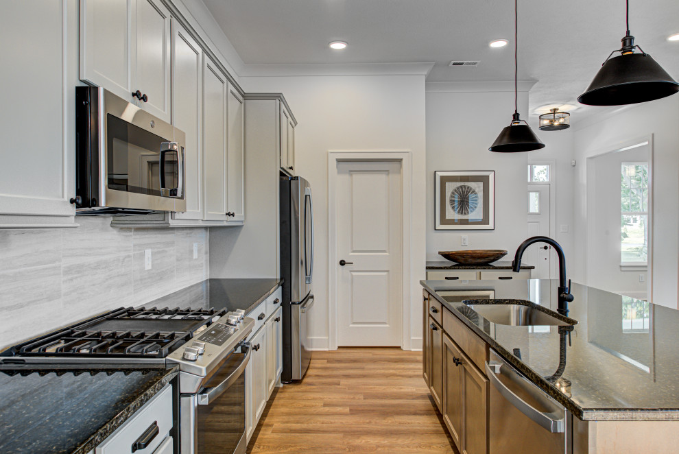Mid-sized arts and crafts galley vinyl floor and brown floor eat-in kitchen photo in Indianapolis with gray backsplash, stainless steel appliances, an island, black countertops, an undermount sink, granite countertops, shaker cabinets, beige cabinets and ceramic backsplash