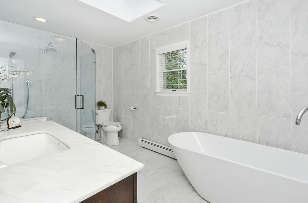 Inspiration for a transitional porcelain tile porcelain tile freestanding bathtub remodel with flat-panel cabinets, dark wood cabinets, a two-piece toilet, an undermount sink, marble countertops and a hinged shower door
