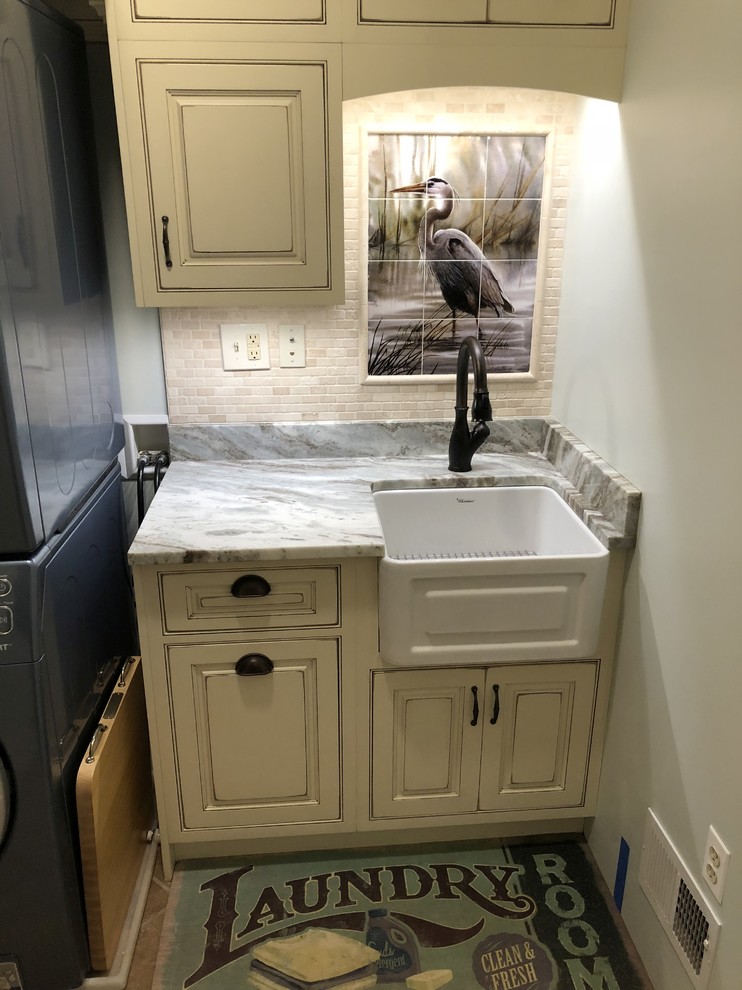 Photo of a small beach style single-wall dedicated laundry room in Baltimore with a farmhouse sink, beaded inset cabinets, distressed cabinets, granite benchtops, green walls, ceramic floors, a stacked washer and dryer, brown floor and brown benchtop.