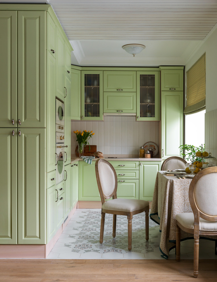 This is an example of a traditional l-shaped open plan kitchen in Moscow with a drop-in sink, raised-panel cabinets, green cabinets, white splashback, white appliances, no island, beige benchtop and multi-coloured floor.