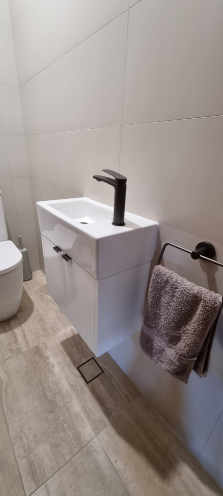 This is an example of a large powder room in Sydney with flat-panel cabinets, white cabinets, a two-piece toilet, beige tile, ceramic tile, beige walls, ceramic floors, an undermount sink, engineered quartz benchtops, beige floor, white benchtops, a floating vanity and recessed.