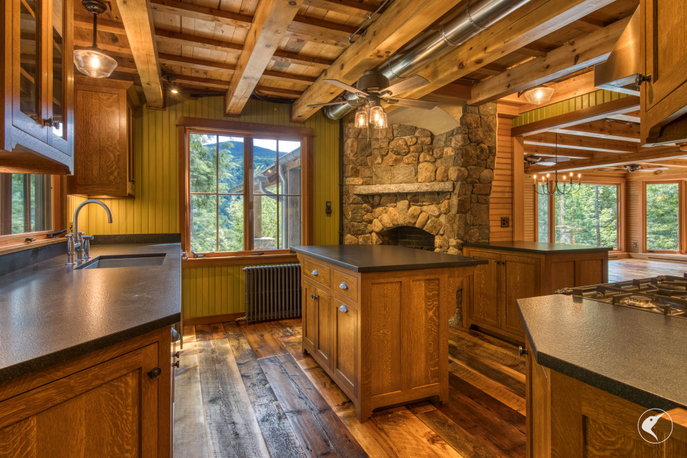 Mountain style medium tone wood floor and exposed beam kitchen photo with an undermount sink, shaker cabinets, granite countertops, black backsplash, granite backsplash, stainless steel appliances, an island and black countertops