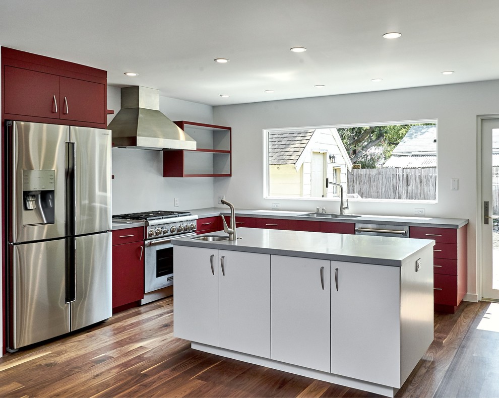 Example of a mid-sized minimalist l-shaped medium tone wood floor and brown floor open concept kitchen design in San Francisco with an undermount sink, flat-panel cabinets, red cabinets, solid surface countertops, stainless steel appliances, an island and gray countertops