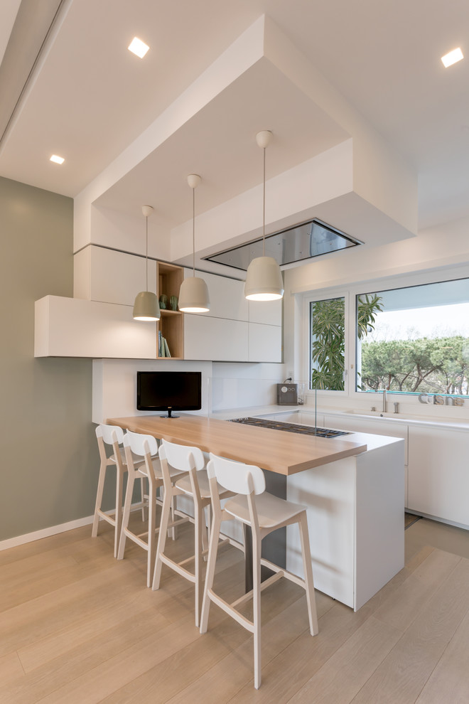 This is an example of a contemporary u-shaped kitchen in Rome with flat-panel cabinets, white cabinets, white splashback, light hardwood floors, glass sheet splashback, a peninsula and white benchtop.