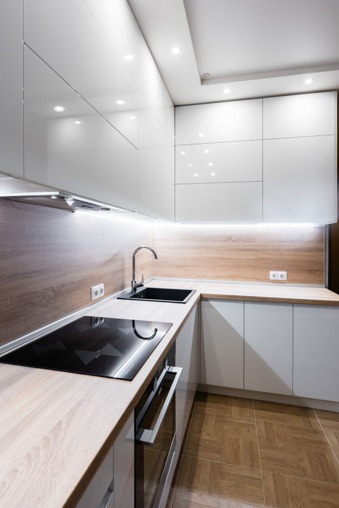 Photo of a medium sized contemporary l-shaped kitchen/diner in Saint Petersburg with a submerged sink, flat-panel cabinets, white cabinets, wood worktops, beige splashback, wood splashback, black appliances, no island and beige worktops.