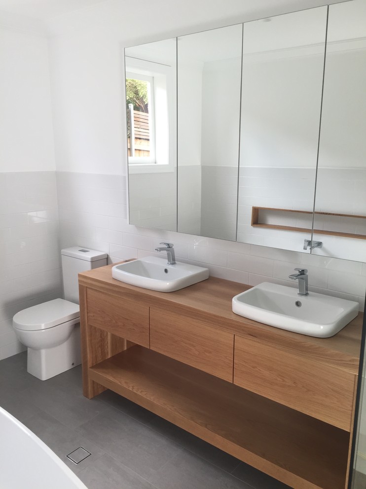 Mid-sized transitional kids bathroom in Sydney with a drop-in sink, recessed-panel cabinets, wood benchtops, a two-piece toilet, white tile, ceramic tile, white walls, ceramic floors, medium wood cabinets and grey floor.