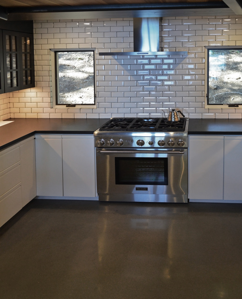 This is an example of a large transitional l-shaped kitchen in Sacramento with white splashback, stainless steel appliances, concrete floors, grey floor, an undermount sink, flat-panel cabinets, white cabinets, solid surface benchtops, subway tile splashback, no island and black benchtop.