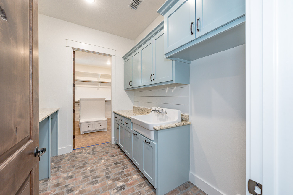 Design ideas for a mid-sized arts and crafts galley dedicated laundry room in Other with a farmhouse sink, shaker cabinets, blue cabinets, granite benchtops, white splashback, shiplap splashback, grey walls, brick floors, a side-by-side washer and dryer, brown floor and beige benchtop.