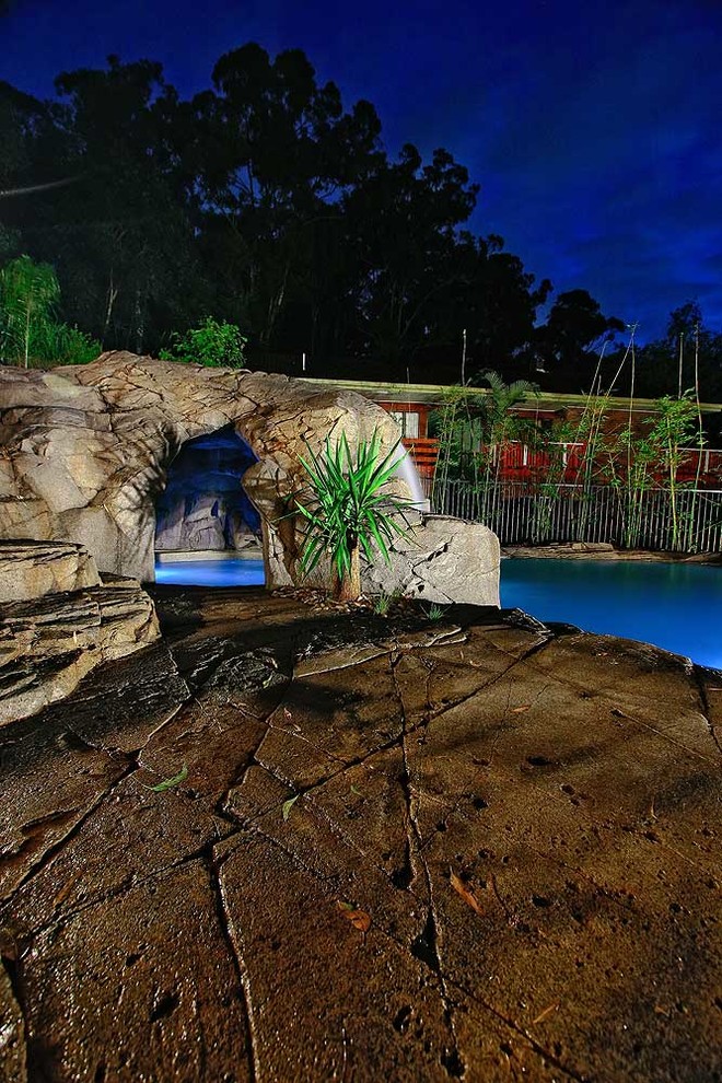 Mid-sized tropical custom-shaped natural pool in Brisbane with a water slide and stamped concrete.
