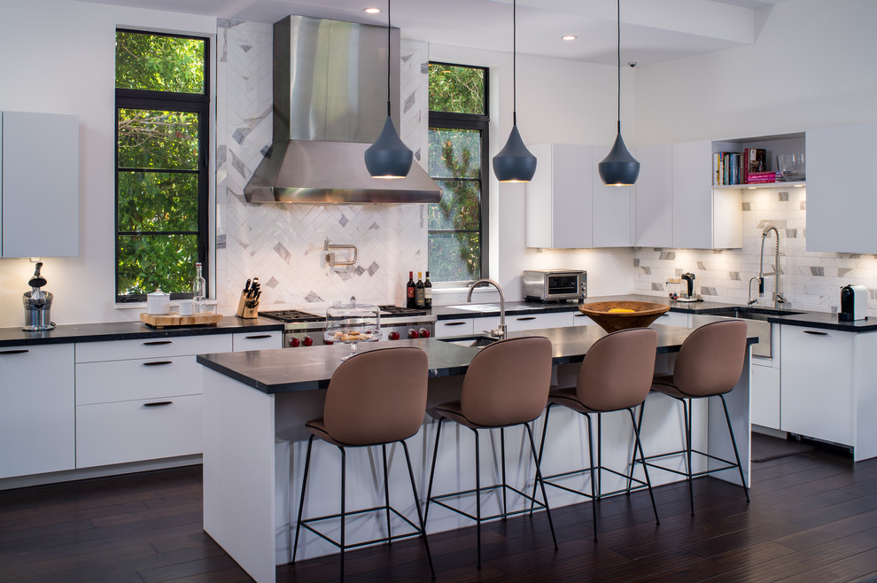 Design ideas for a mid-sized contemporary galley eat-in kitchen in Miami with flat-panel cabinets, white splashback, stainless steel appliances, dark hardwood floors, with island, a farmhouse sink, solid surface benchtops, stone tile splashback and black benchtop.