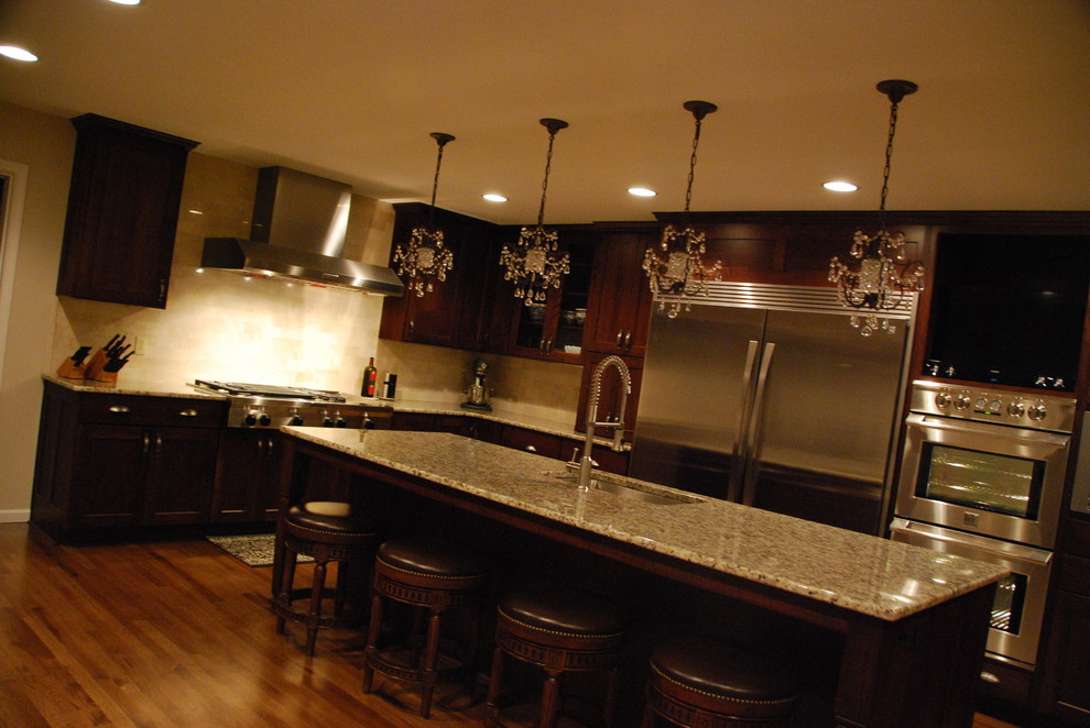 Open concept kitchen - large contemporary l-shaped medium tone wood floor open concept kitchen idea with an undermount sink, recessed-panel cabinets, dark wood cabinets, granite countertops, beige backsplash, stone tile backsplash, stainless steel appliances and two islands