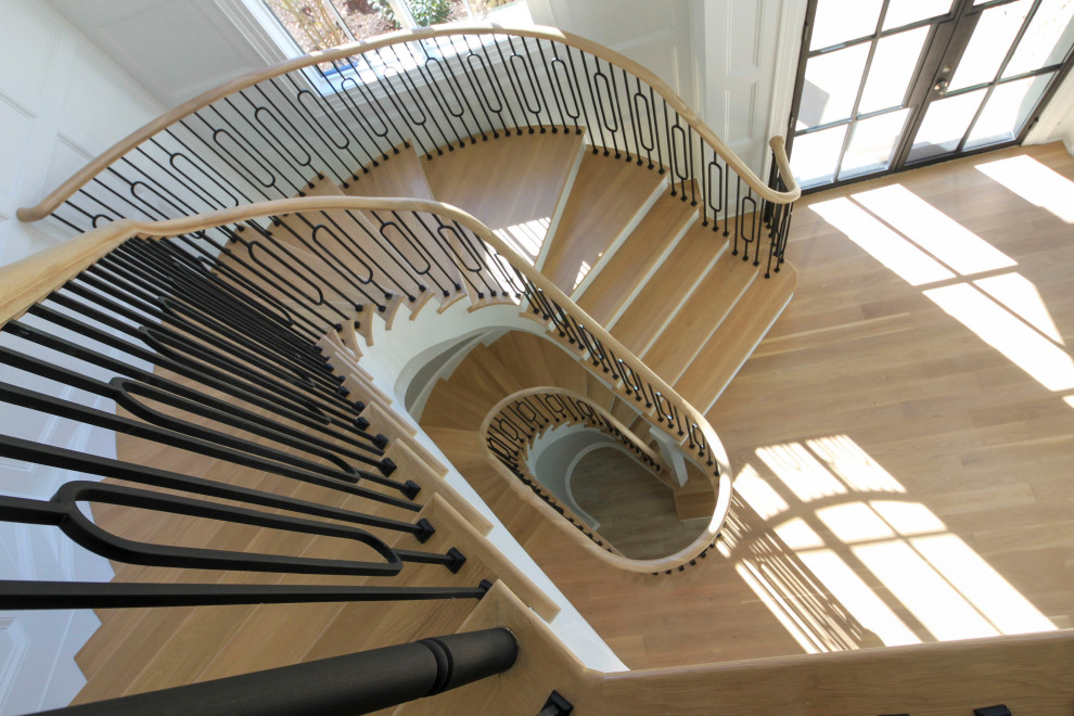 Идея дизайна: огромная изогнутая деревянная лестница в стиле неоклассика (современная классика) с деревянными ступенями, перилами из смешанных материалов и панелями на стенах