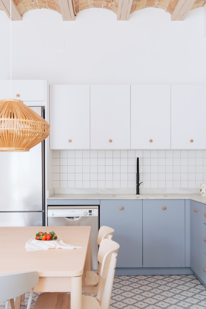 This is an example of a large urban l-shaped open plan kitchen in Valencia with a single-bowl sink, flat-panel cabinets, blue cabinets, marble worktops, white splashback, ceramic splashback, stainless steel appliances, ceramic flooring, blue floors, white worktops and a vaulted ceiling.