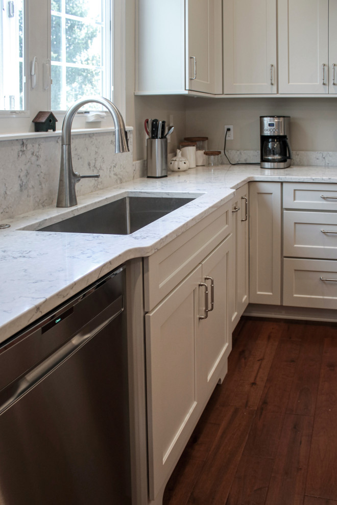 Inspiration for a mid-sized transitional l-shaped eat-in kitchen in Cleveland with a double-bowl sink, flat-panel cabinets, white cabinets, quartz benchtops, white splashback, engineered quartz splashback, stainless steel appliances, medium hardwood floors, with island, brown floor and white benchtop.
