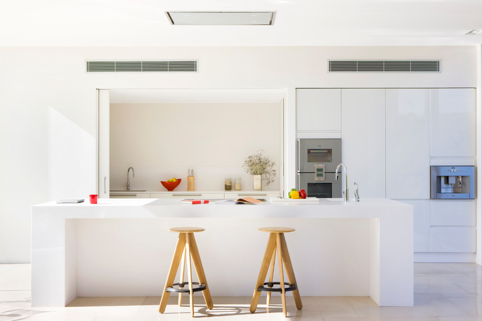 Mid-sized contemporary galley eat-in kitchen in Other with an integrated sink, flat-panel cabinets, white cabinets, solid surface benchtops, white splashback, stainless steel appliances, travertine floors and with island.