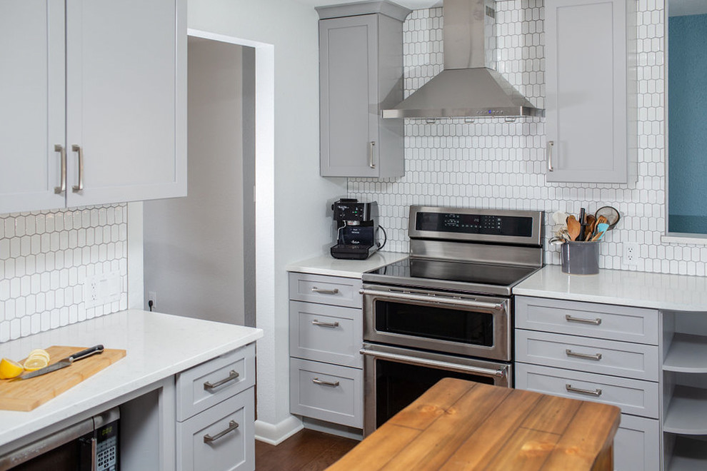 This is an example of a mid-sized transitional galley eat-in kitchen in Denver with an undermount sink, shaker cabinets, grey cabinets, quartz benchtops, white splashback, ceramic splashback, stainless steel appliances, medium hardwood floors, with island, brown floor and white benchtop.