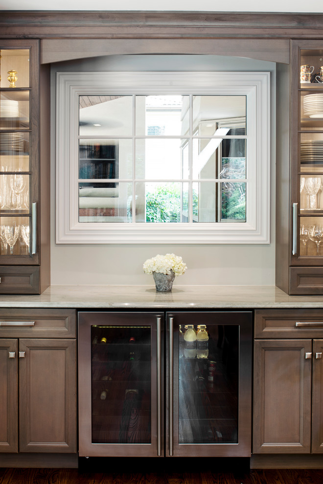 Inspiration for a large transitional single-wall medium tone wood floor and brown floor kitchen remodel in Denver with an undermount sink, recessed-panel cabinets, brown cabinets, white backsplash, stone slab backsplash, stainless steel appliances and an island