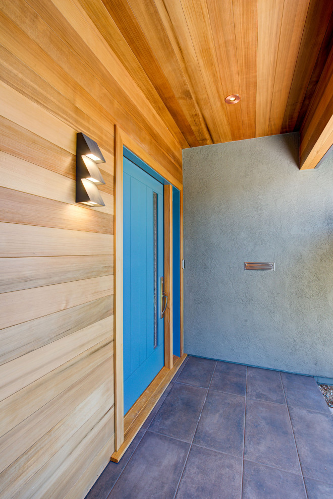 Exempel på en retro entré, med en pivotdörr, en blå dörr och brunt golv